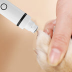The grinder head of the Still Wagging Quiet Body Shaver being used on a dog's nail, with the paw held steady in one hand